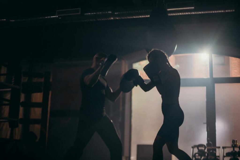 Silhouetted boxers sparring during an intense training session in a dimly lit gym.